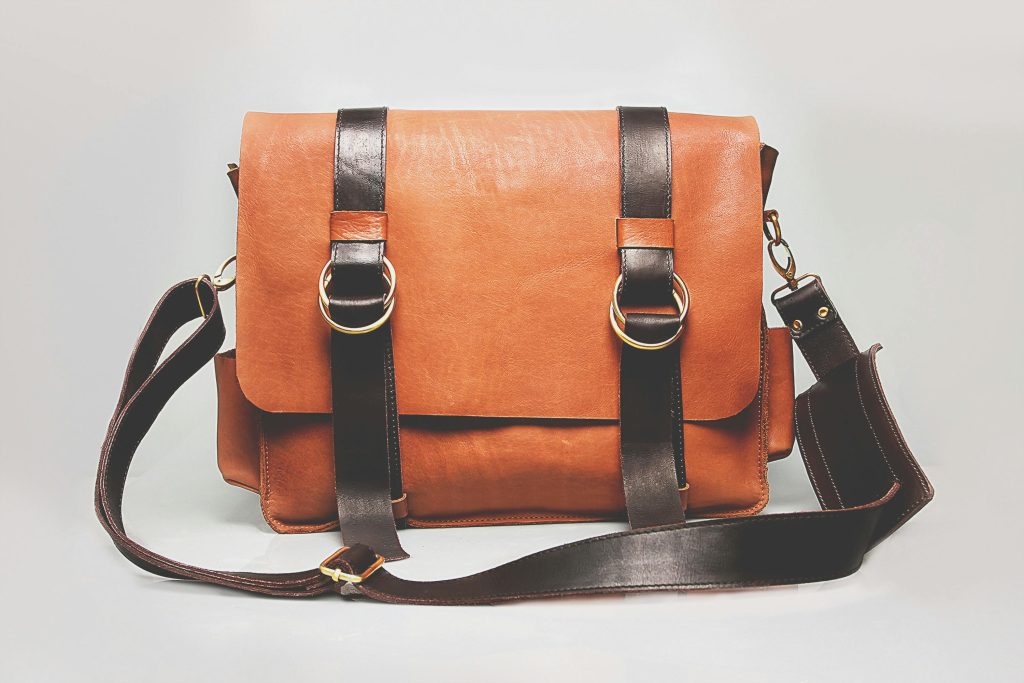 Elegant brown leather briefcase with dark straps and metal buckles, ideal for fashion and business.